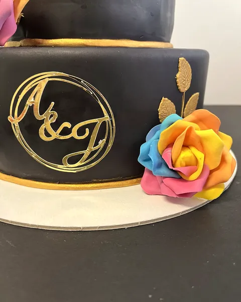 Tarta negra con iniciales doradas y rosa multicolor